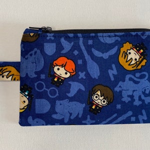 May include: A blue zippered pouch with a Harry Potter themed print featuring characters like Harry Potter, Ron Weasley, and Hermione Granger. The pouch has a key ring attached.