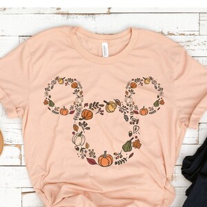 May include: A heather peach t-shirt with a fall-themed Mickey Mouse silhouette. The silhouette is made up of leaves, pumpkins, and acorns.