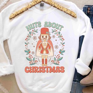 May include: White sweatshirt with a Christmas-themed graphic featuring a nutcracker doll and the text "Nuts About Christmas".