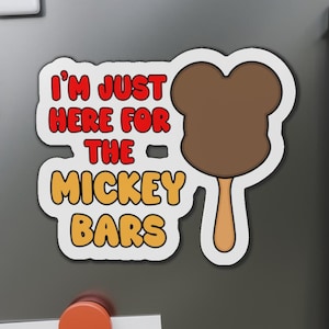 May include: A white magnet with the text "I'M JUST HERE FOR THE MICKEY BARS" in red and yellow. A brown Mickey Mouse ice cream bar graphic is on the right side of the magnet.