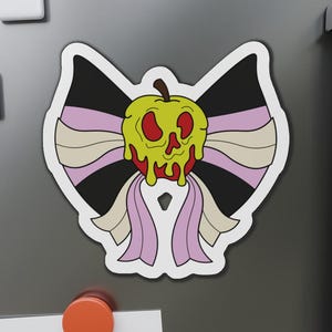 Puede incluir: Un imán troquelado con una imagen de dibujos animados de una manzana envenenada. La manzana es amarilla con detalles rojos y gotea, sobre un lazo negro y rosa. El imán está adherido a un refrigerador gris.