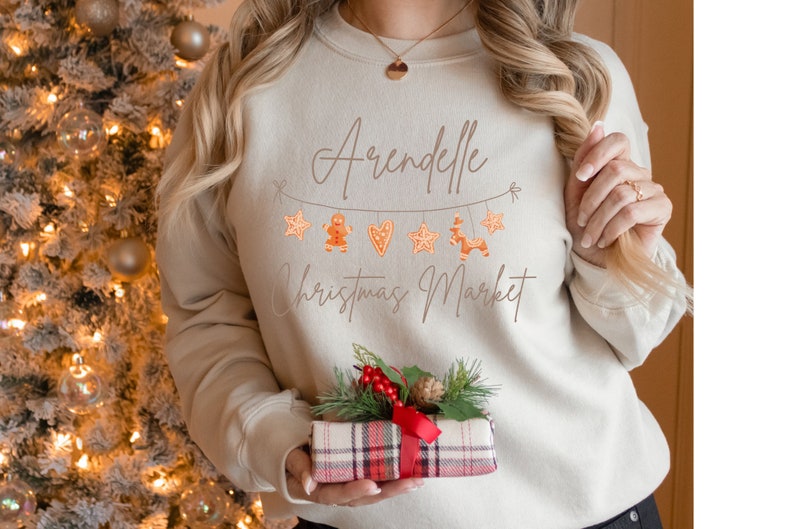 May include: A beige sweatshirt with the text "Arendelle Christmas Market" and a string of gingerbread cookies, stars, and hearts.