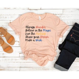 May include: A peach-colored t-shirt with the text "Always Wonder Believe in the Magic Live the Fantasy Share your Dream Make a Wish" printed in colorful letters.