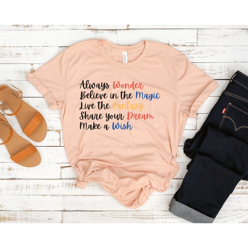 May include: A peach-colored t-shirt with the text "Always Wonder Believe in the Magic Live the Fantasy Share your Dream Make a Wish" printed in colorful letters.