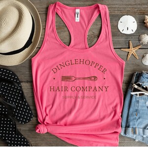 Peut inclure: Un d&eacute;bardeur rose avec un graphique brun qui dit "Dinglehopper Hair Company Supply & Service" avec un graphique de fourchette.