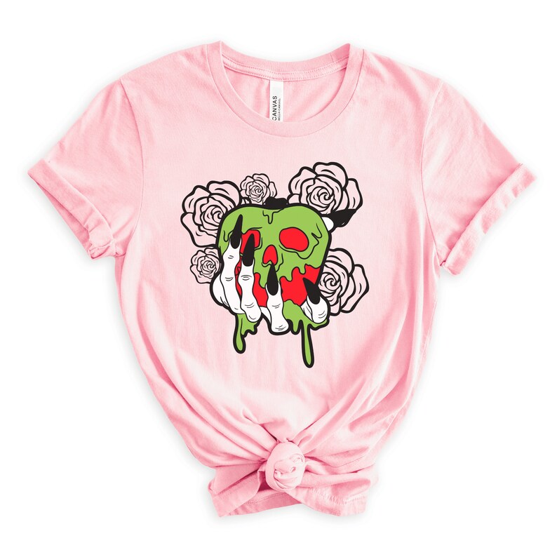 Pu&ograve; includere: Maglietta rosa con una mela verde e rossa con un viso di teschio e gocciolamenti di melma verde. Una mano scheletrica con lunghi artigli neri tiene la mela. Ci sono rose bianche intorno alla mela.