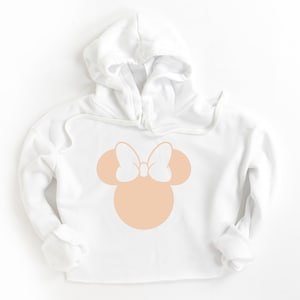 Puede incluir: Sudadera con capucha blanca con una silueta de Minnie Mouse de color melocot&oacute;n con un lazo blanco.