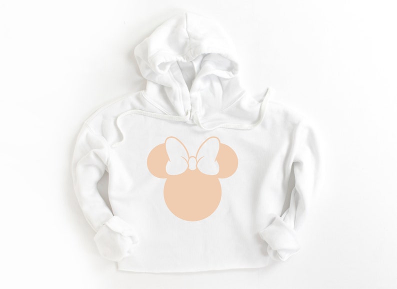 Puede incluir: Sudadera con capucha blanca con una silueta de Minnie Mouse de color melocot&oacute;n con un lazo blanco.