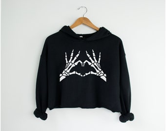 May include: Black cropped hoodie with a white skeleton hand design making a heart shape.