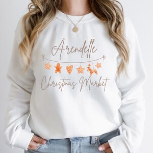 May include: White sweatshirt with a brown graphic design that says "Arendelle Christmas Market" with gingerbread cookies and stars hanging from a string.
