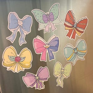 Puede incluir: Conjunto de nueve imanes de colores en forma de lazo con varios diseños, incluyendo una mariposa, una corona y una perla. Los imanes son perfectos para añadir un toque de fantasía a cualquier refrigerador o superficie metálica.