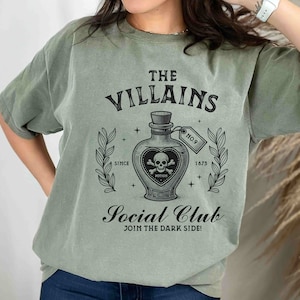 May include: A green t-shirt with a vintage-style graphic of a potion bottle with a skull and crossbones. The text reads "The Villains Social Club, Join the Dark Side!"