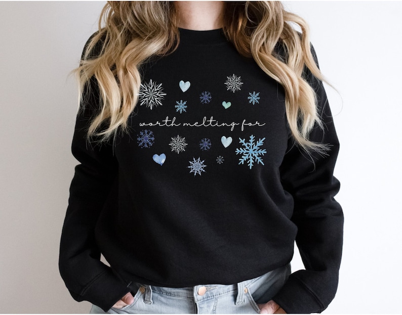 Puede incluir: Sudadera negra con un gr&aacute;fico blanco que dice "worth melting for" y dise&ntilde;os azules de copos de nieve y corazones.