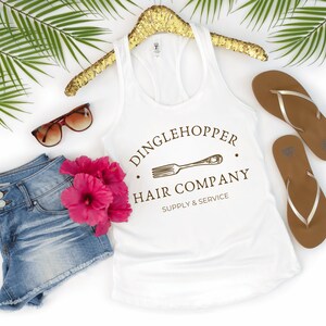 Peut inclure: Un d&eacute;bardeur blanc avec un graphique brun qui dit "Dinglehopper Hair Company Supply & Service" avec un dessin d'une fourchette.