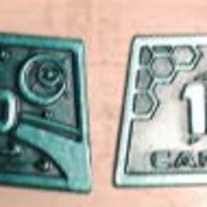 May include: Two silver-colored metal tokens with the number 100 on them. The token on the left has a blue-green color and a design of a planet and stars. The token on the right has a hexagonal design and the word "EAF" on it.