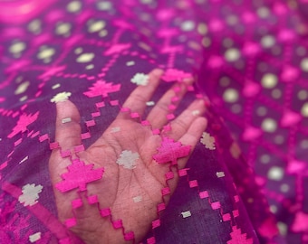 May include: Close-up of a sheer fabric with a vibrant pattern. The fabric features a deep purple base with a repeating design of pink and white floral and geometric shapes. The fabric is draped, creating folds and shadows.