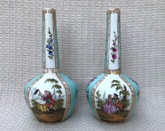 May include: Two porcelain vases with a turquoise glaze and gold accents. Each vase features a hand-painted scene of a couple in a garden setting. The vases have a slender neck and a rounded body.