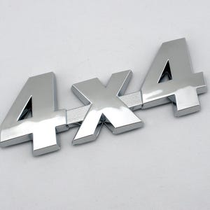 Puede incluir: Un brillante emblema 4x4 cromado, ideal para vehículos. El emblema presenta los números y la letra "X" en una fuente audaz y en bloque. El emblema está diseñado para montarse en un vehículo.
