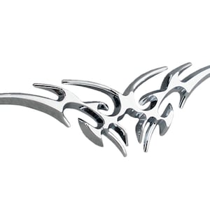 May include: A chrome-finished decorative emblem with a tribal flame design. The symmetrical piece features curved, pointed shapes that extend outwards from a central point. The shiny, metallic surface reflects light, creating highlights and shadows.