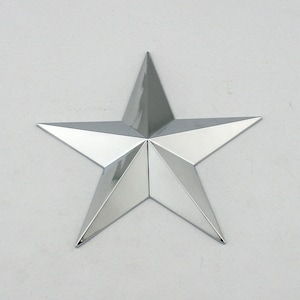 May include: A shiny, silver five-pointed star. The star has a reflective surface and is mounted on a white background. The star's points are sharp and well-defined, creating a striking visual effect. This decorative star could be used as a wall decoration.