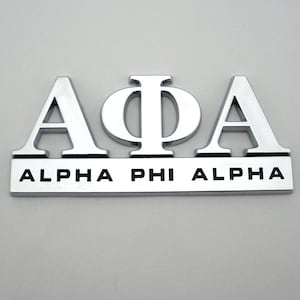 May include: A shiny, silver emblem featuring the Greek letters Alpha, Phi, and Alpha, with the words "ALPHA PHI ALPHA" below. The letters are raised and have a reflective surface, set against a plain background.