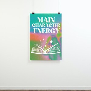 May include: A poster with a colorful, abstract background featuring a white open book with stars above it. The text "MAIN CHARACTER ENERGY" is written in white letters on the poster.