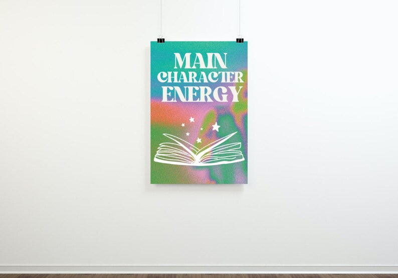 May include: A poster with a colorful, abstract background featuring a white open book with stars above it. The text "MAIN CHARACTER ENERGY" is written in white letters on the poster.