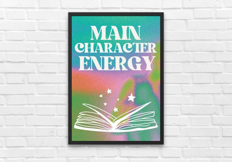 May include: A framed print with a colorful background and the text "MAIN CHARACTER ENERGY" in white. A white outline of an open book with stars above it is in the center of the print.