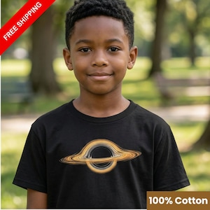 Può includere: T-shirt nero con grafica di un buco nero con dettagli arancioni e bianchi. La maglietta è realizzata in 100% cotone. L'immagine include anche il testo "FREE SHIPPING" e "100% Cotton".