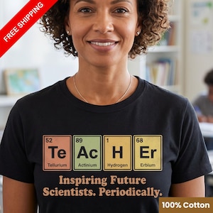 May include: A black short-sleeve t-shirt featuring a graphic of four periodic table elements spelling the word Teacher. The elements are Tellurium, Actinium, Hydrogen, and Erbium. Below the graphic is the text Inspiring Future Scientists. Periodically.