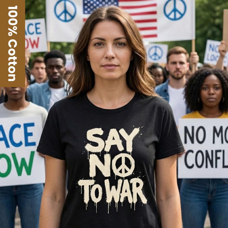 May include: A black t-shirt with the text "SAY NO TO WAR" in a dripping font, featuring a peace symbol. The shirt is made of 100% cotton. People are in the background holding signs and an American flag.