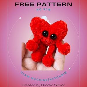 May include: A red crocheted heart-shaped plush toy with black eyes. The toy is being held in a hand and is labeled "Claw Machine/Keychain". The text "HEART BUDDY FREE PATTERN NO SEW" is at the top of the image. The text "Created by Brooke Skiver @lilnellieknits" is at the bottom of the image.