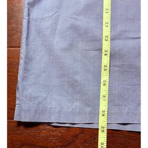 K&ouml;nnte beinhalten: Ein Abschnitt hellblauen Stoffes mit einem Gittermuster, gemessen mit einem gelben Ma&szlig;band. Das Ma&szlig;band zeigt eine L&auml;nge von ca. 76 cm. Der Stoff liegt auf einer dunkelbraunen Holzoberfl&auml;che.