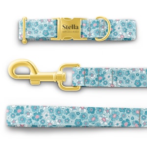 K&ouml;nnte beinhalten: Ein blaues und wei&szlig;es Blumen-Hundehalsband und eine Leine mit goldenen Beschl&auml;gen. Das Halsband hat ein personalisiertes Namensschild mit der Aufschrift "Stella" und einer Telefonnummer.