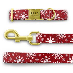 Peut inclure: Ensemble collier et laisse pour chien rouge avec un motif de flocons de neige blancs. Le collier a une boucle dor&eacute;e avec le nom "LUCY" et le num&eacute;ro de t&eacute;l&eacute;phone "419.555.0322" grav&eacute;s dessus.