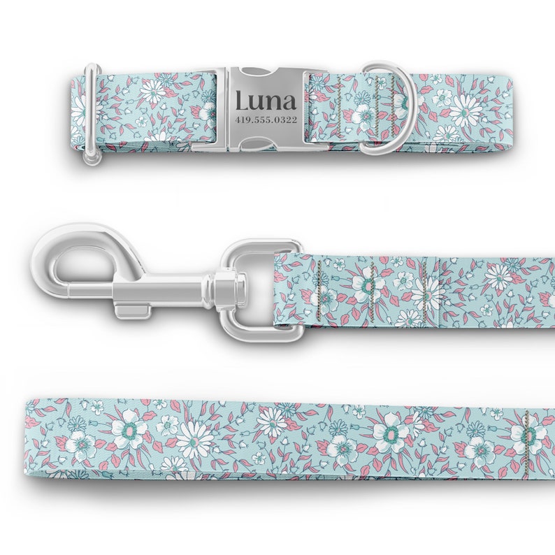 K&ouml;nnte beinhalten: Ein hellblaues Hundehalsband und eine Leine mit einem wei&szlig;en Blumenmuster. Das Halsband hat eine silberne Schnalle mit dem Namen "Luna" und einer eingravierten Telefonnummer.