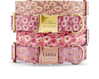 May include: Three pink dog collars with a daisy print. The top collar has a gold buckle with the name "Willow" and phone number "419.555.0322" engraved on it. The middle collar has a gold buckle. The bottom collar has a rose gold buckle with the name "Luna" and phone number "419.555.0322" engraved on it.