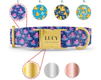 May include: A blue dog collar with a pink rubber ducky pattern and a gold buckle. The buckle has the name "LUCY" and the phone number "419.555.0322" engraved on it. The collar is shown with three different buckle color options: gold, silver, and rose gold.