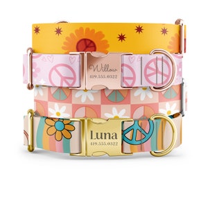 May include: Three dog collars with peace sign and flower patterns. The top collar is yellow with a sunflower and stars. The middle collar is pink with peace signs and hearts. The bottom collar is peach with rainbow stripes and daisies. Each collar has a gold buckle with a name and phone number engraved on it. The names are "Willow" and "Luna".