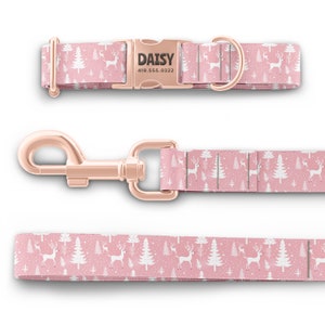 May include: A pink dog collar and leash set with a white reindeer and pine tree pattern. The collar has a rose gold buckle with the name "DAISY" and phone number "419.555.0322" engraved on it.