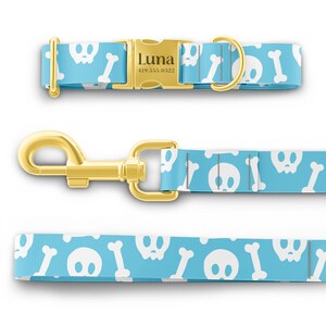 K&ouml;nnte beinhalten: Ein blaues Hundehalsband mit einem wei&szlig;en Totenkopf- und Knochenmuster. Das Halsband hat eine goldene Schnalle mit dem Namen "Luna" und einer eingravierten Telefonnummer.