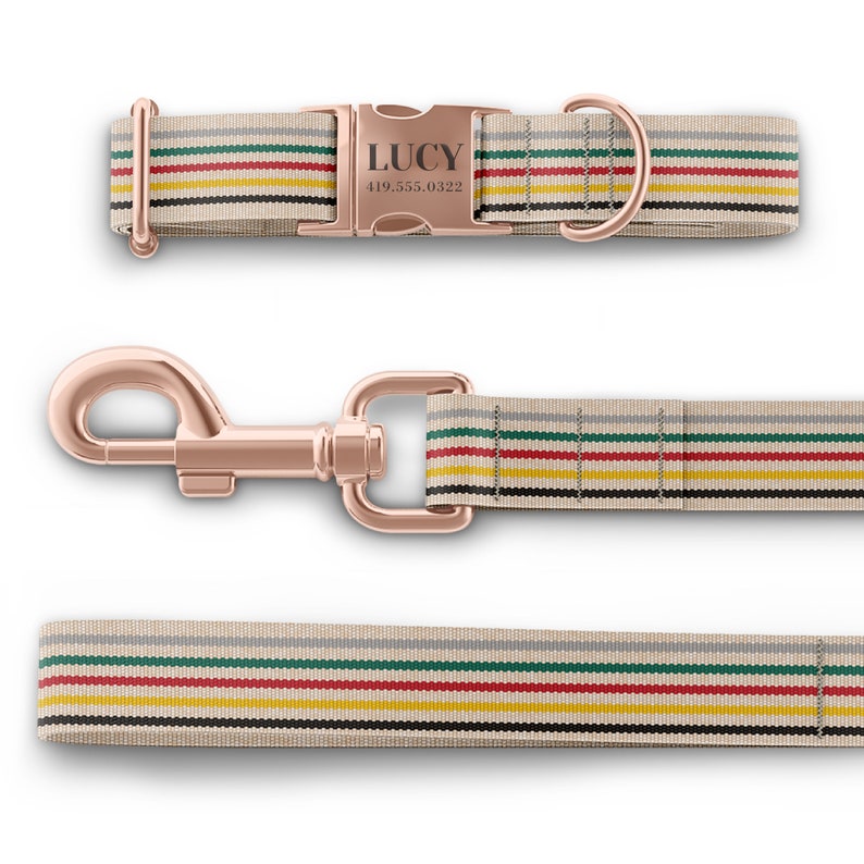 May include: A dog collar and leash set with a beige background and horizontal stripes in red, green, yellow, and black. The collar has a rose gold buckle engraved with "LUCY" and a phone number. The leash has a matching rose gold clasp.