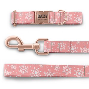 Peut inclure: Un collier et une laisse pour chien rose avec un motif de flocons de neige blancs. Le collier a une boucle en or rose avec le nom "DAISY" et un num&eacute;ro de t&eacute;l&eacute;phone grav&eacute; dessus. La laisse a un mousqueton en or rose.