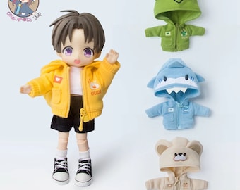 May include: Four hooded jackets for dolls, each with a different animal design: a green frog, a blue shark, a beige bear, and a yellow duck. The jackets have zipper closures and pockets.