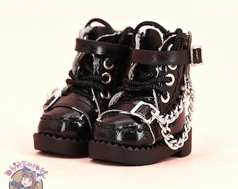 May include: Black leather doll boots with silver buckles and a silver chain detail. The boots have laces and a chunky heel.
