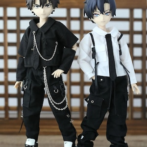 May include: Two fashion dolls wearing black cargo trousers and trainers. One doll is wearing a black shirt with a silver chain, and the other doll is wearing a white shirt with a black tie.