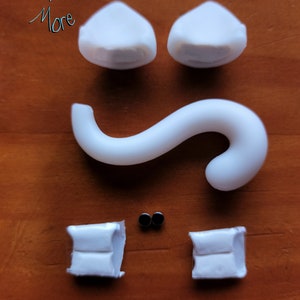 May include: White plastic pieces for a DIY cat figurine kit. The kit includes two ears, a tail, two feet, and two black eyes.