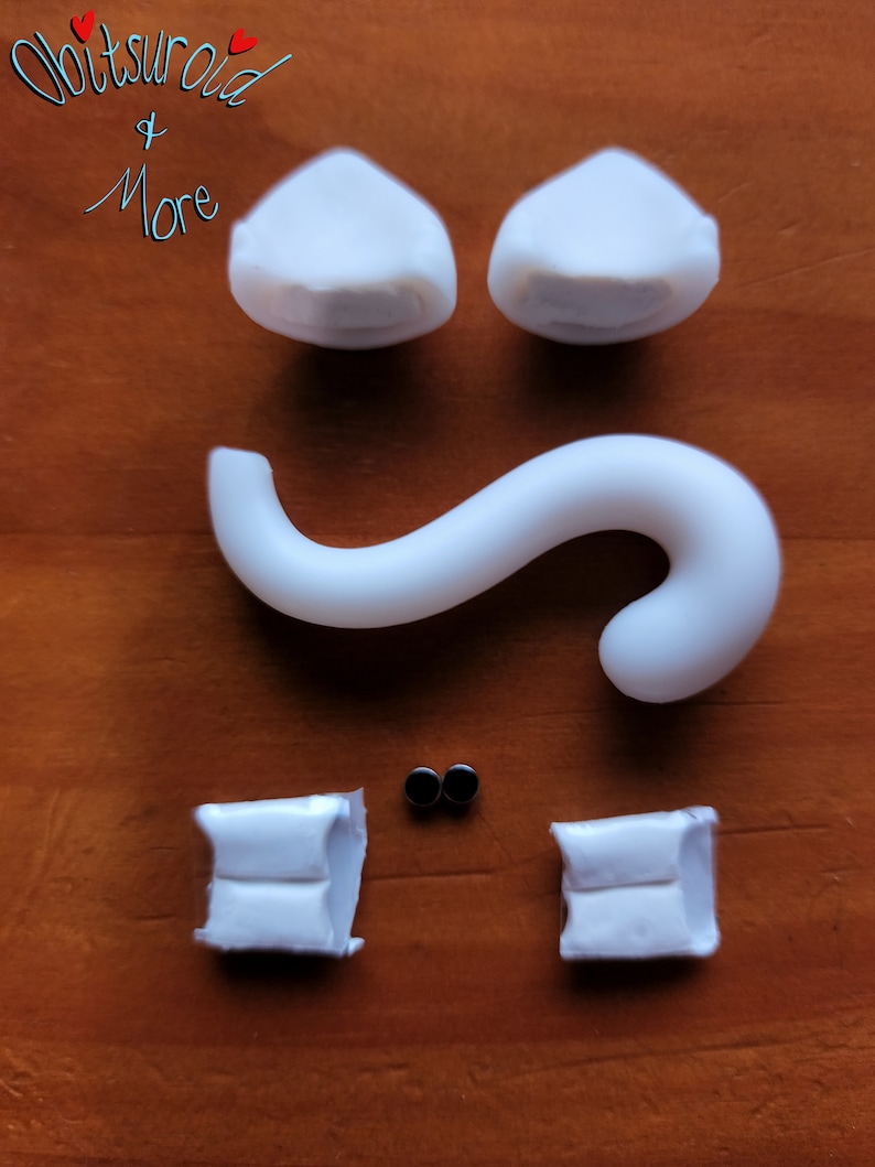 May include: White plastic pieces for a DIY cat figurine kit. The kit includes two ears, a tail, two feet, and two black eyes.