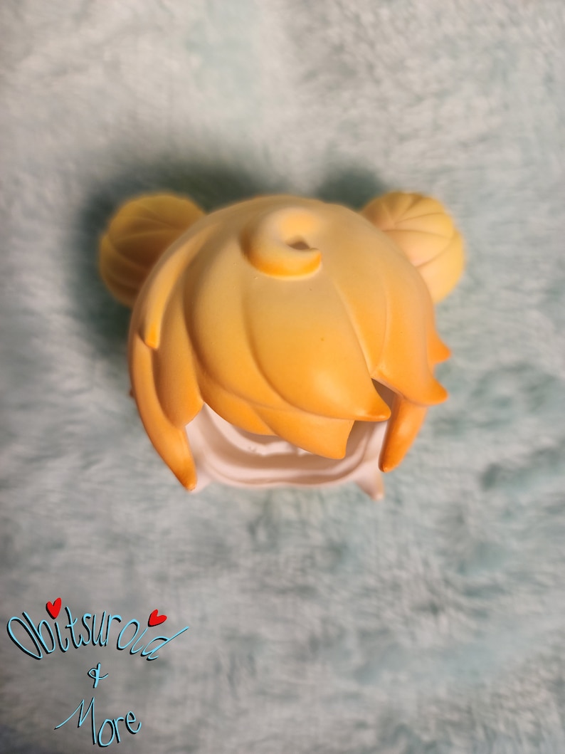 May include: A yellow doll hair wig with two buns on top. The wig is made of a soft, pliable material and is designed to fit a doll's head.
