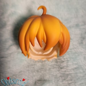 May include: A yellow-orange doll hair wig with a pumpkin shape. The wig is made of a soft, smooth material and has a natural-looking texture.